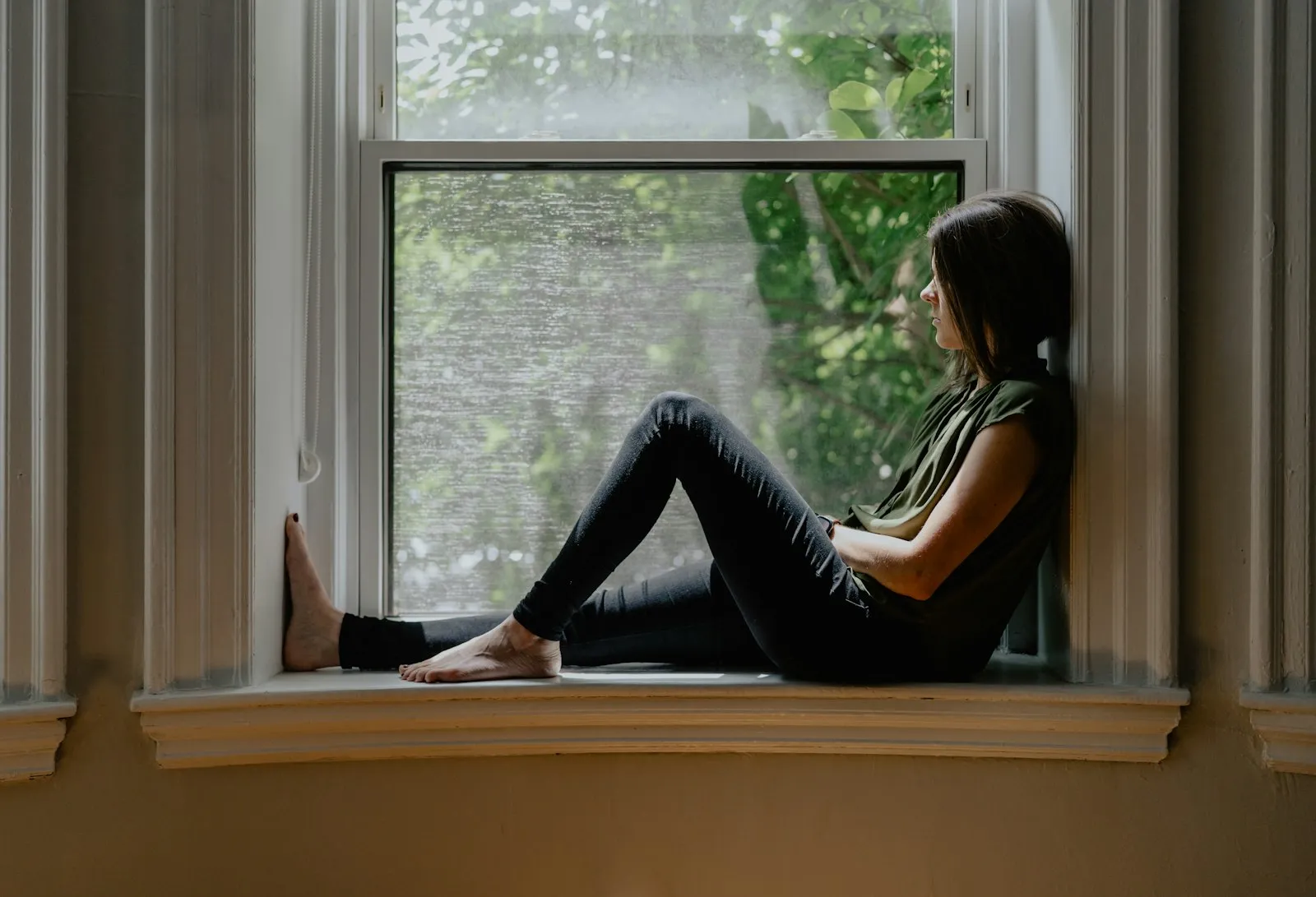 Mujer sentada en el marco de una ventana, tranquila